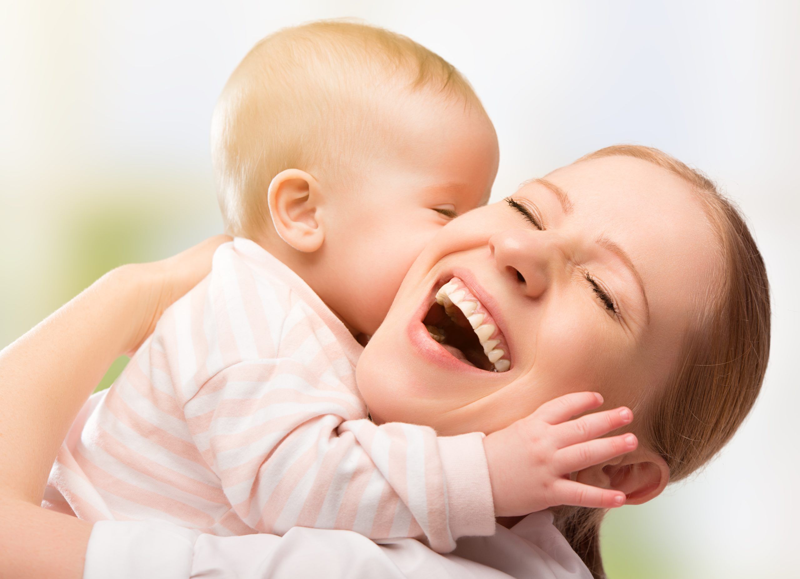 A woman is caressing a baby and smiling with an open mouth.