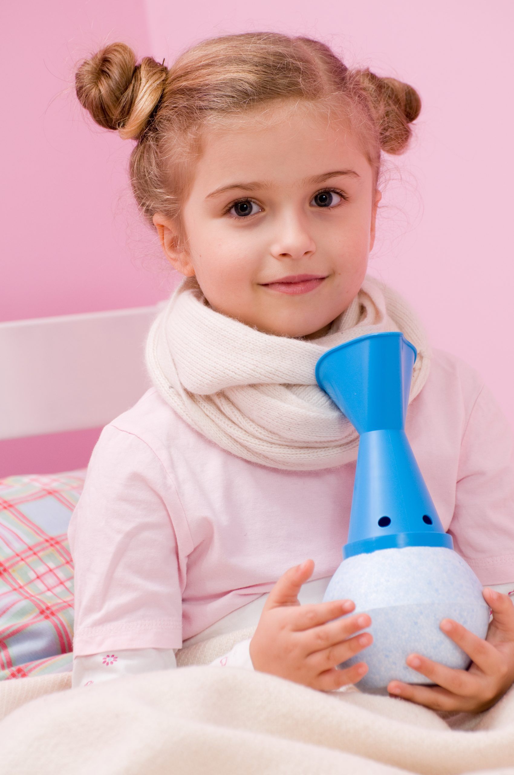 A little girl in a pink bedroom is holding a blue nebulizer to treat asthma.