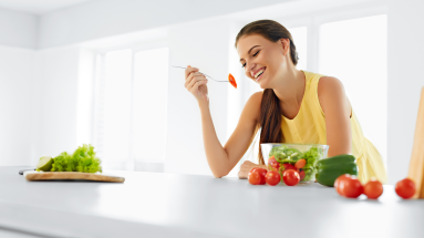 A woman in a white kitchen sits at the counter with a bowl of salad.
