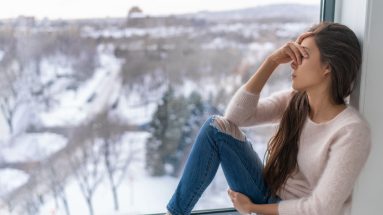 A woman sits on a windowsill with a snowy winter scene in the background.