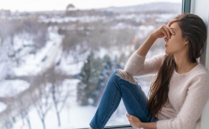 A woman sits on a windowsill with a snowy winter scene in the background.