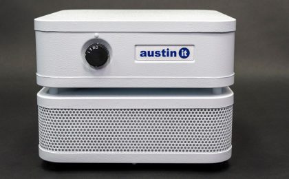Close up image of the Austin “it” personal air purifier. “it” is a white, rectangular steel appliance with grating on the bottom half and a solid panel with a control switch is on top. The tag says, “Austin it” in blue print.