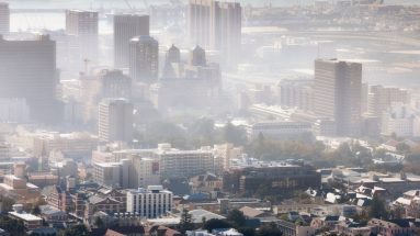 A photo of a cityscape in the daytime in the sunshine but the sky is thick with smog.