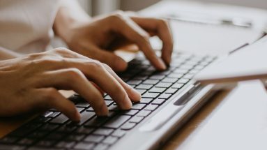 A close up photo featuring a pair of hands typing on a sleek, black keyboard.