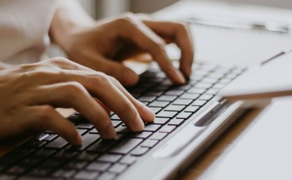 A close up photo featuring a pair of hands typing on a sleek, black keyboard.