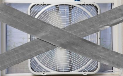 A photo of a box fan in a window with a large “X” made of duct tape going over the length of the image.
